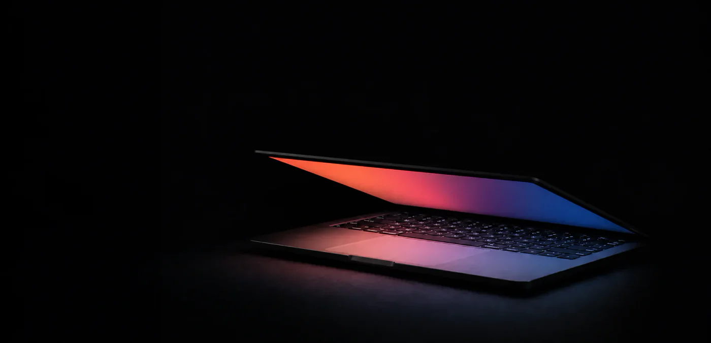 MacBook Air partly open in a dark room, with its colorful screen illuminating the keyboard