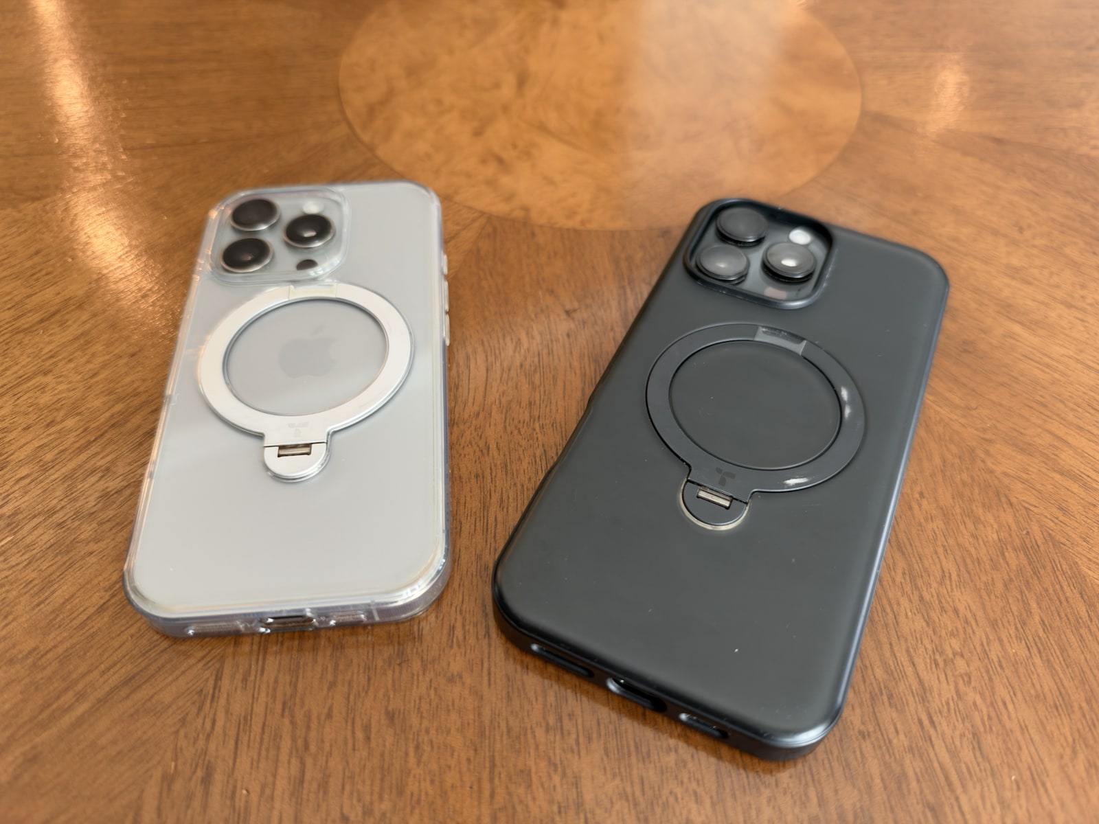 Clear and black Torras Q3 cases lying flat on a wooden table, showing worn paint on the darker kickstand ring after two years.