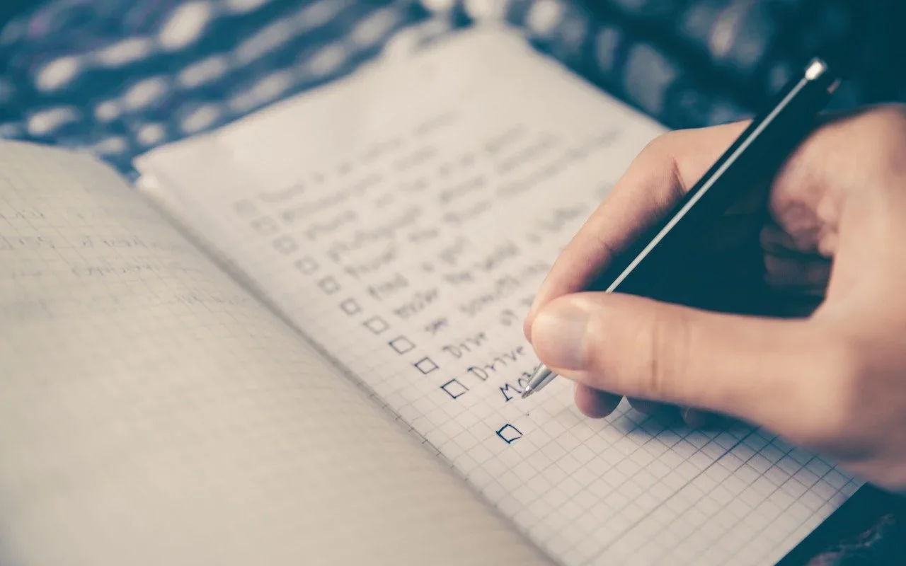 A hand checking items on a paper to-do list