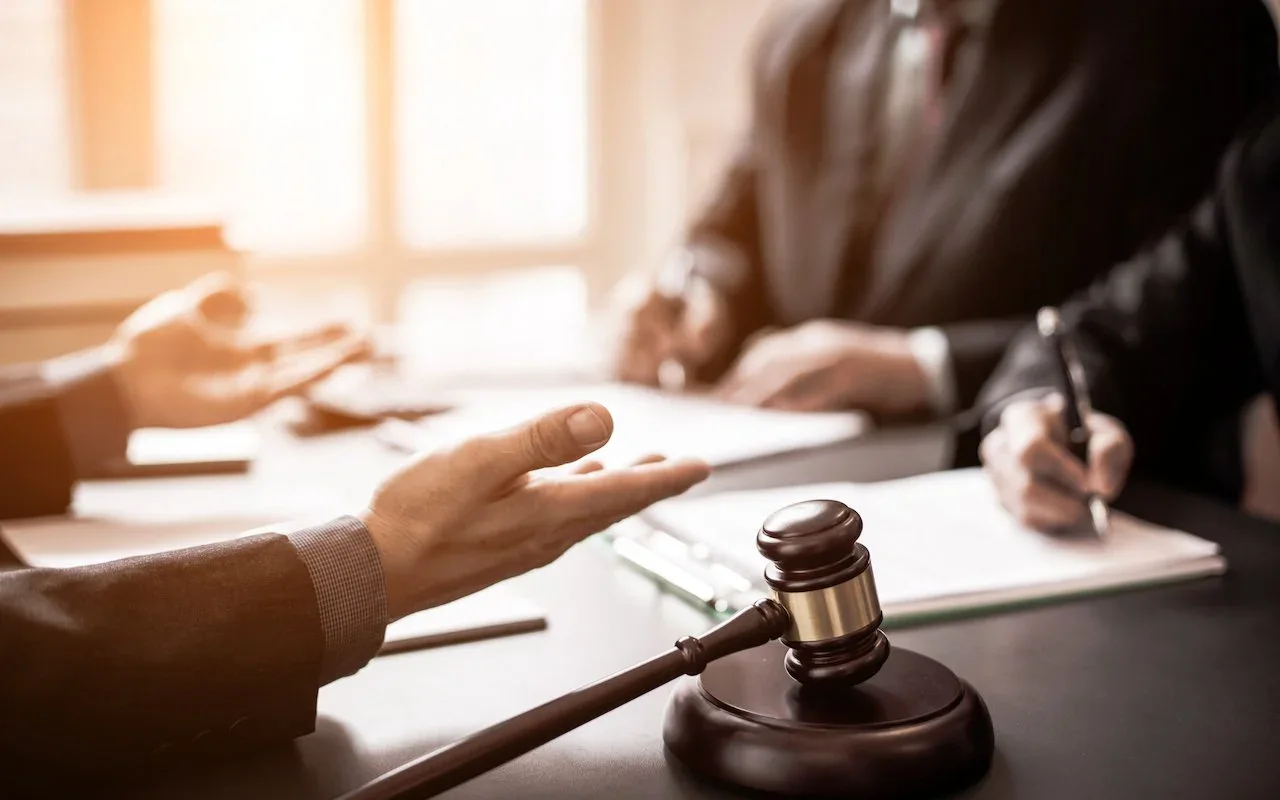 A lawyer and client signing paperwork beside a judge's gavel