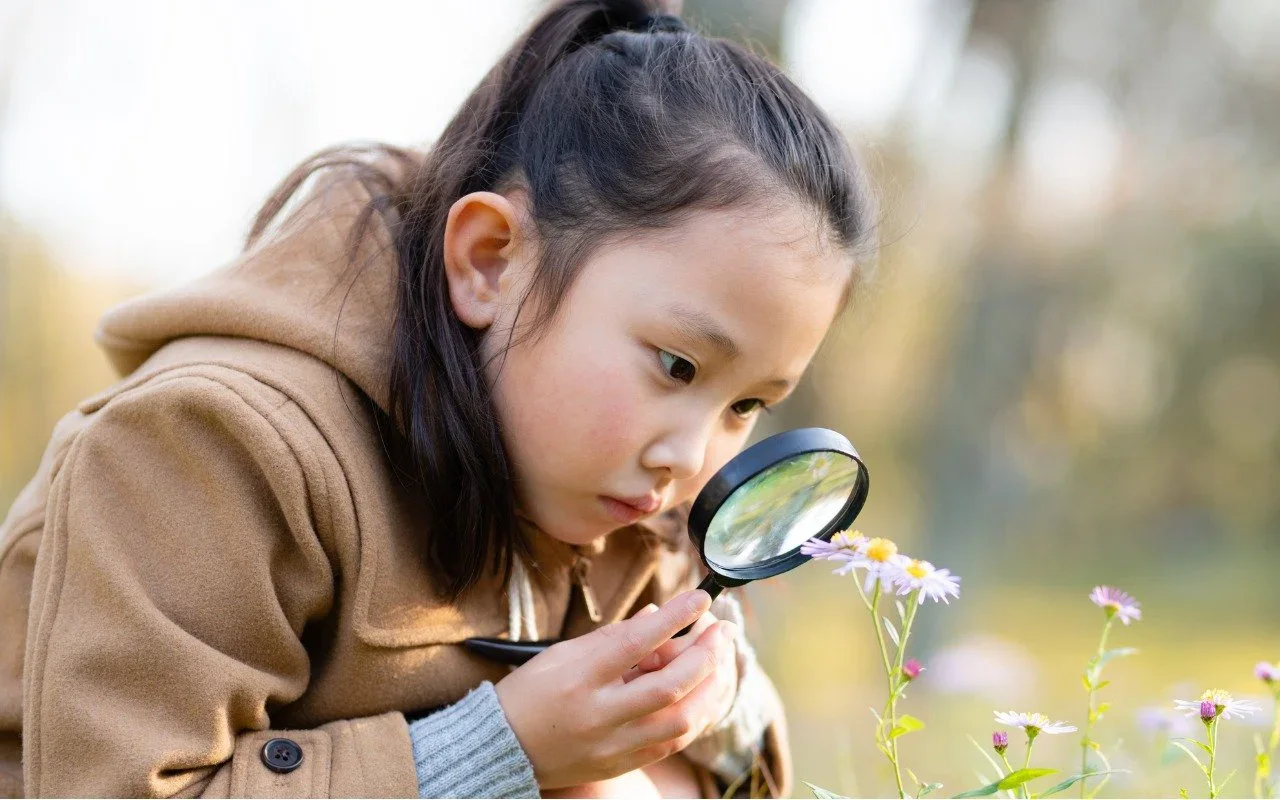 A child examining a flower through a magnifying glass