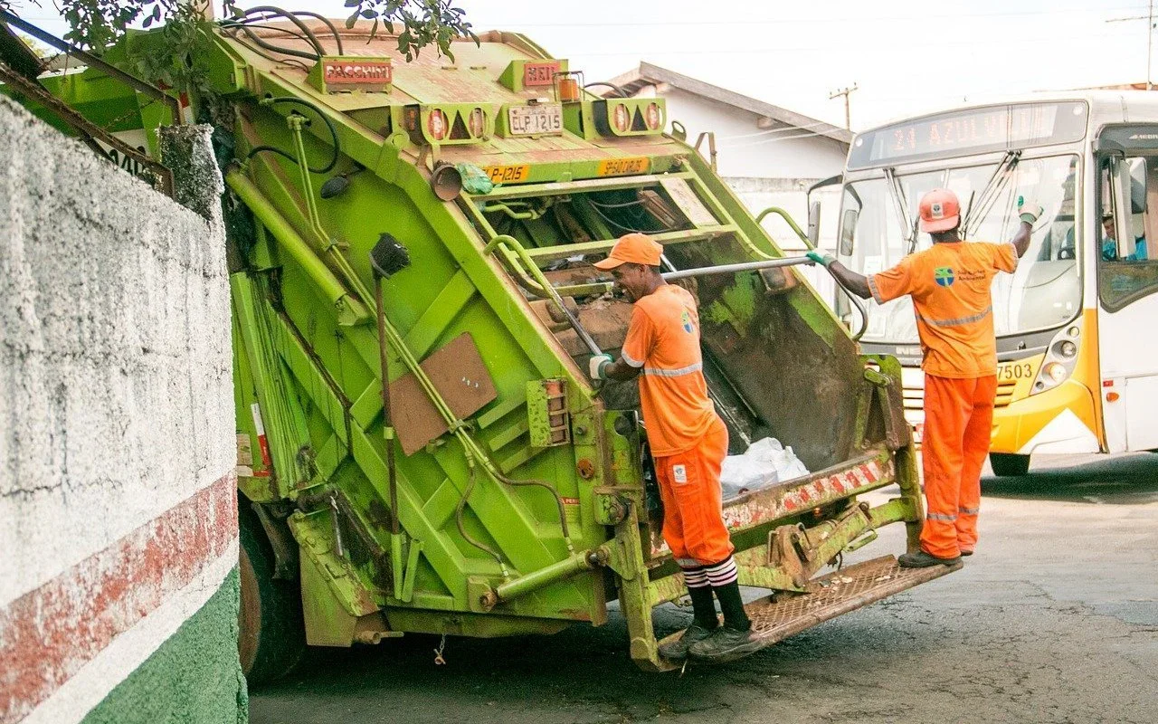 Sanitation workers loading a green garbage truck