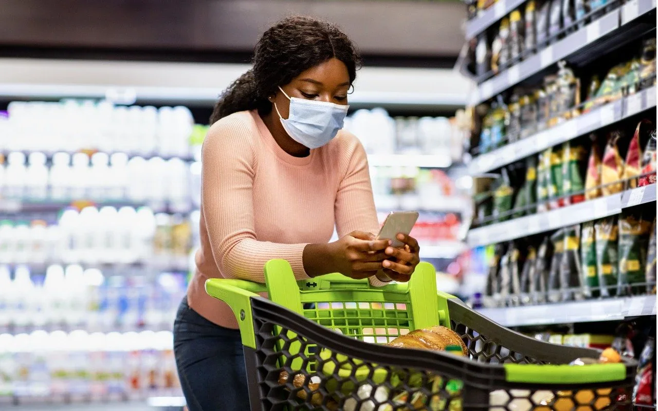 A masked shopper looking at her phone in a grocery store