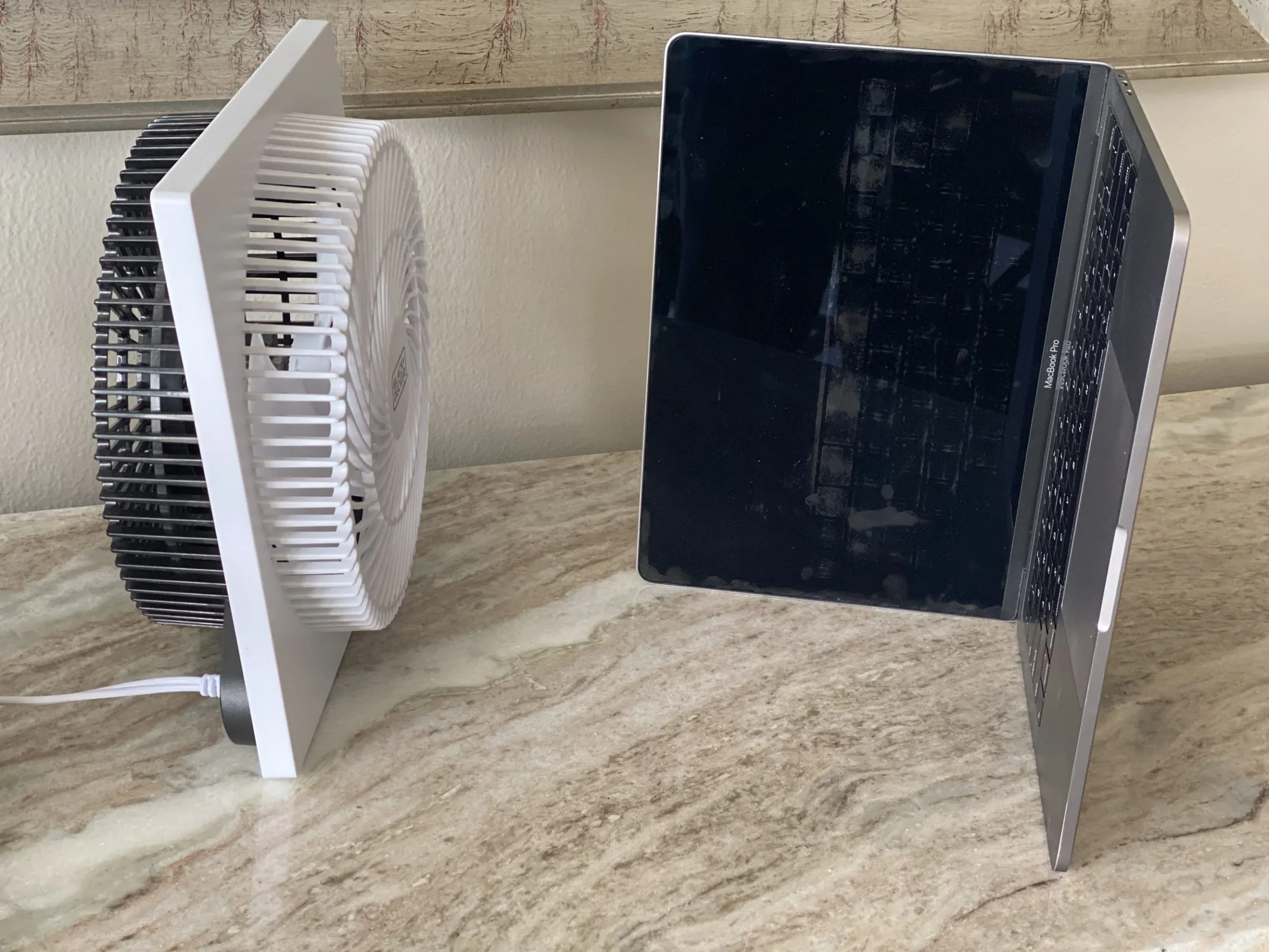 A wet MacBook propped open beside a fan to dry