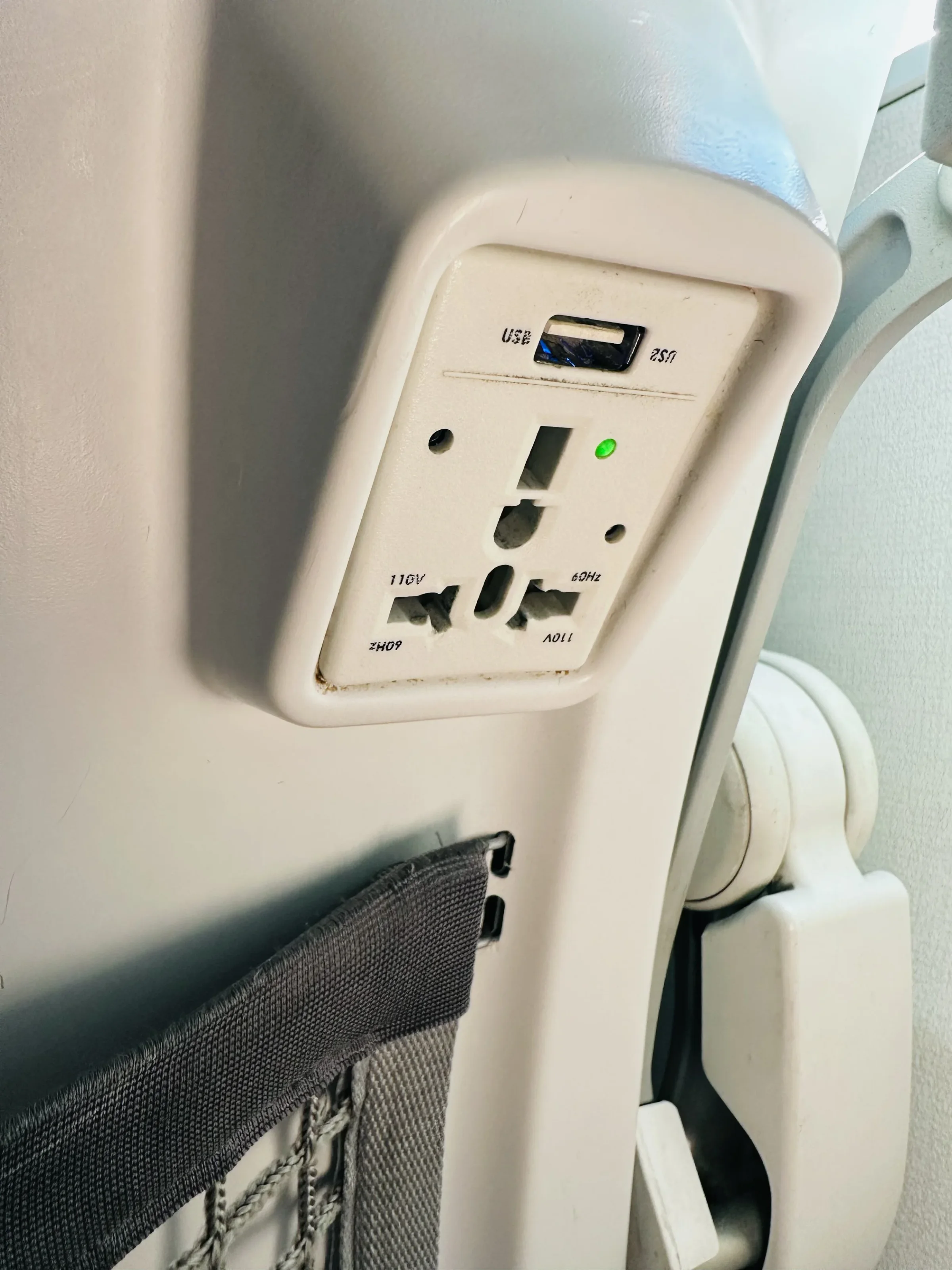 An Alaska Airlines universal power outlet mounted on an airplane seat