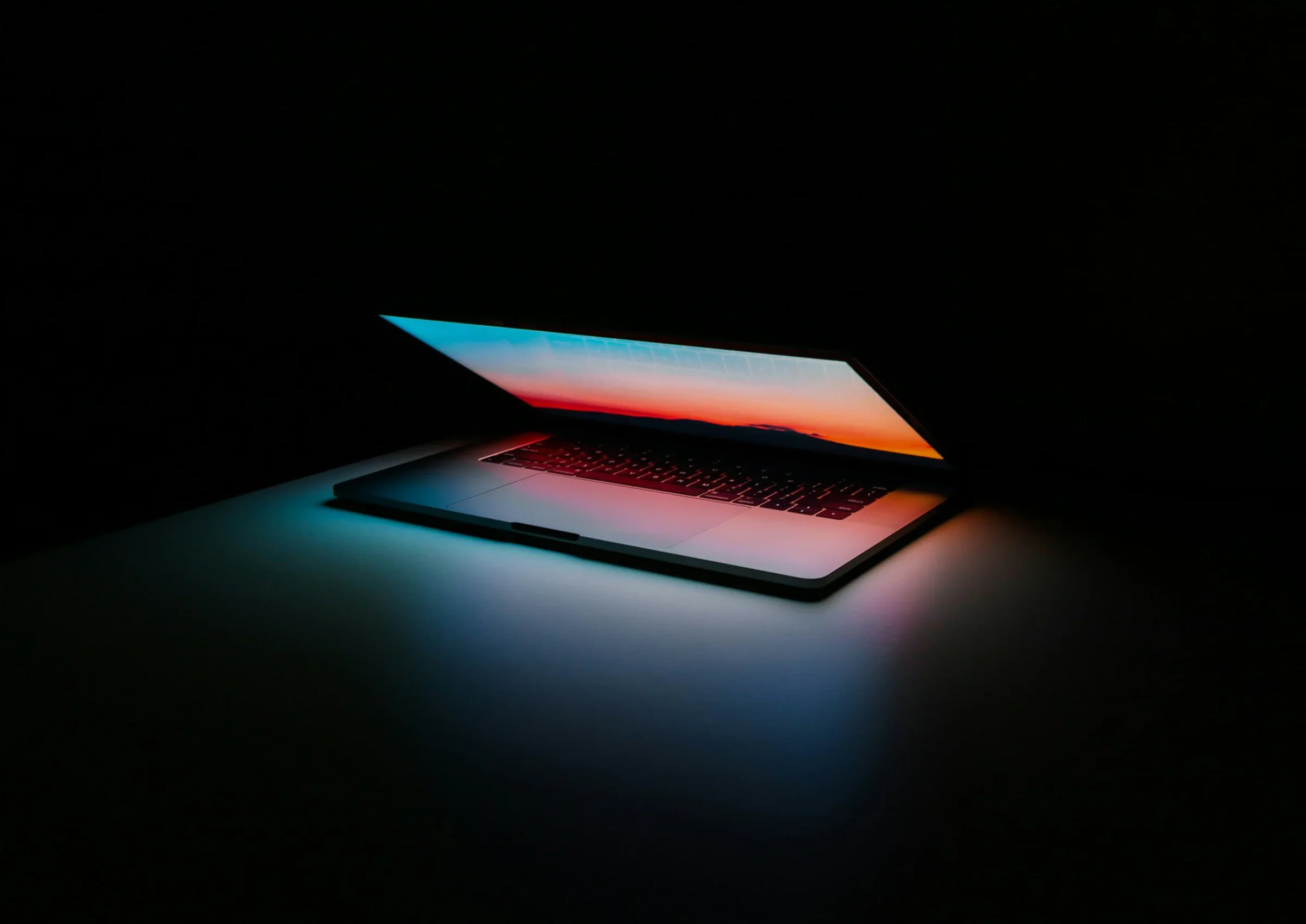 A partially open MacBook illuminated by blue, red, and orange light in a dark room