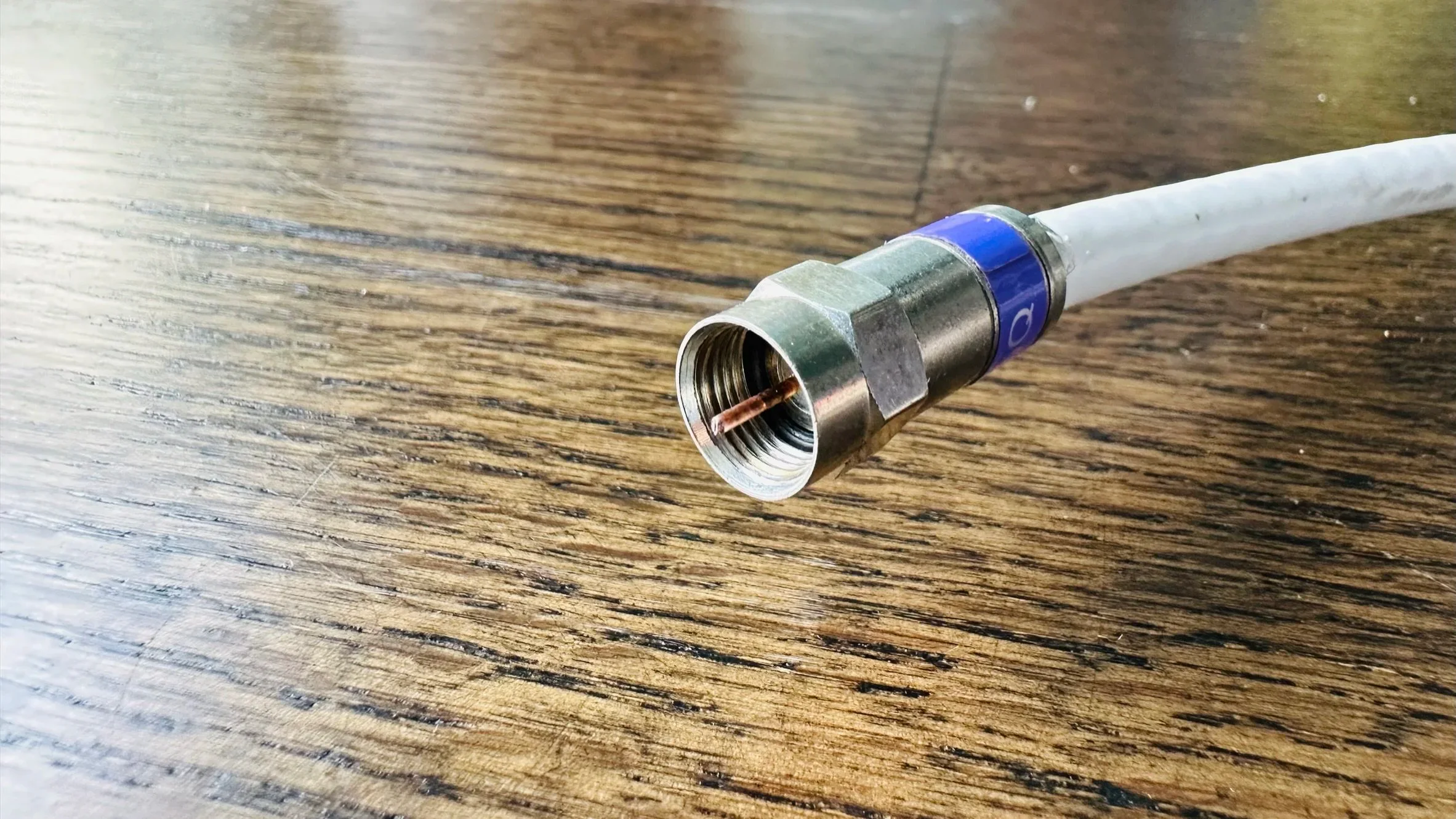 Close-up of a coaxial cable connector screwing into a white wall port