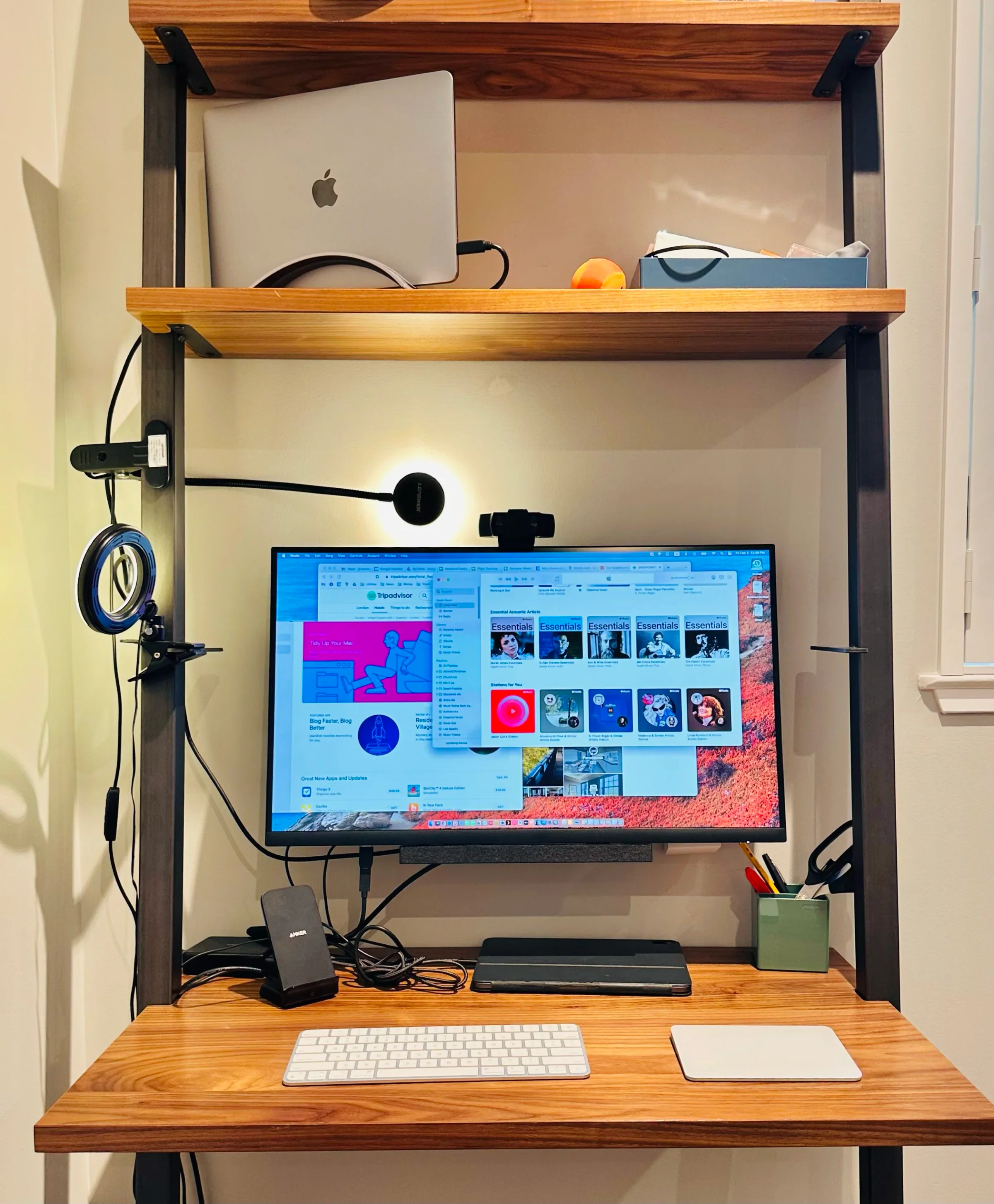 A closed MacBook Pro in a vertical Book Arc stand next to a 27-inch monitor, with a Logitech webcam, Magic Keyboard, and Magic Trackpad
