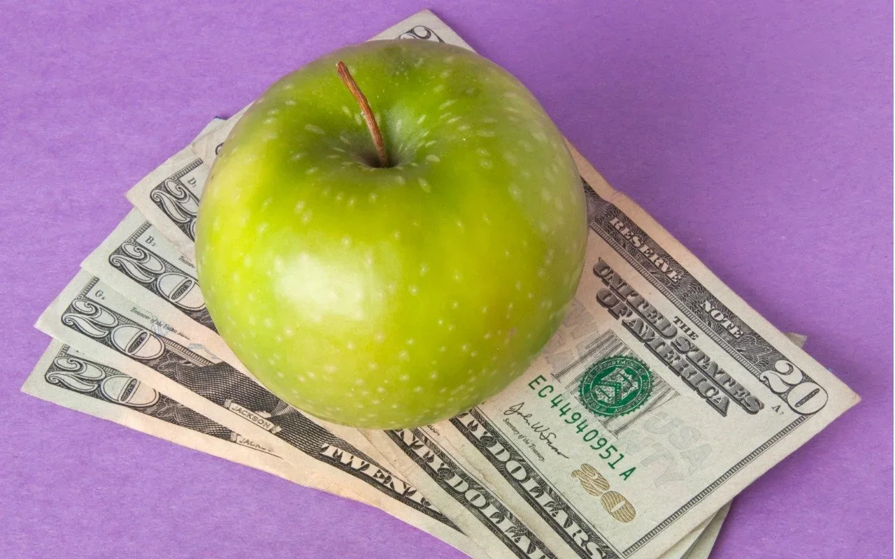 Green apple resting on a fan of dollar bills