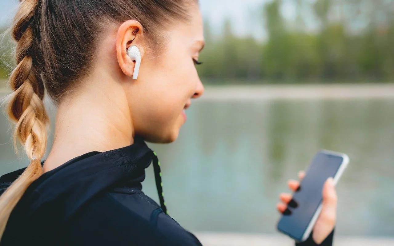 A woman wearing AirPods while looking at her iPhone outdoors