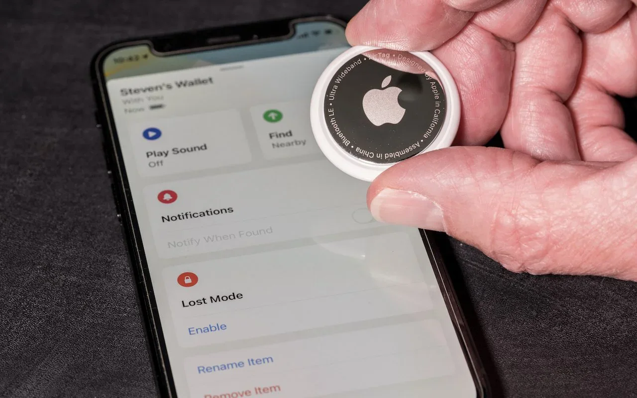 A hand holding an AirTag above an iPhone displaying its safety options