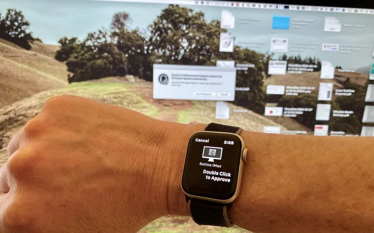 Apple Watch displaying an approval request while worn on a wrist beside a Mac