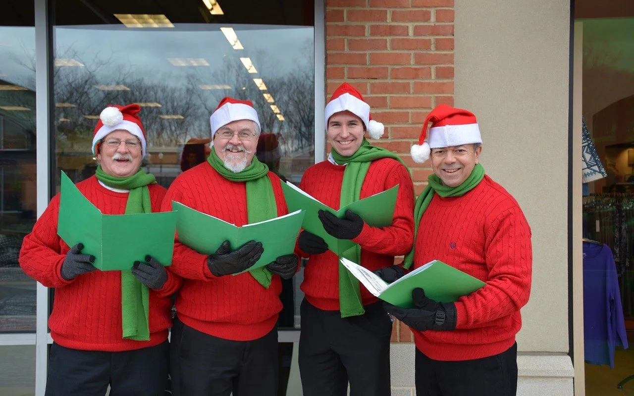 Four people wearing elf hats and singing Christmas carols from songbooks