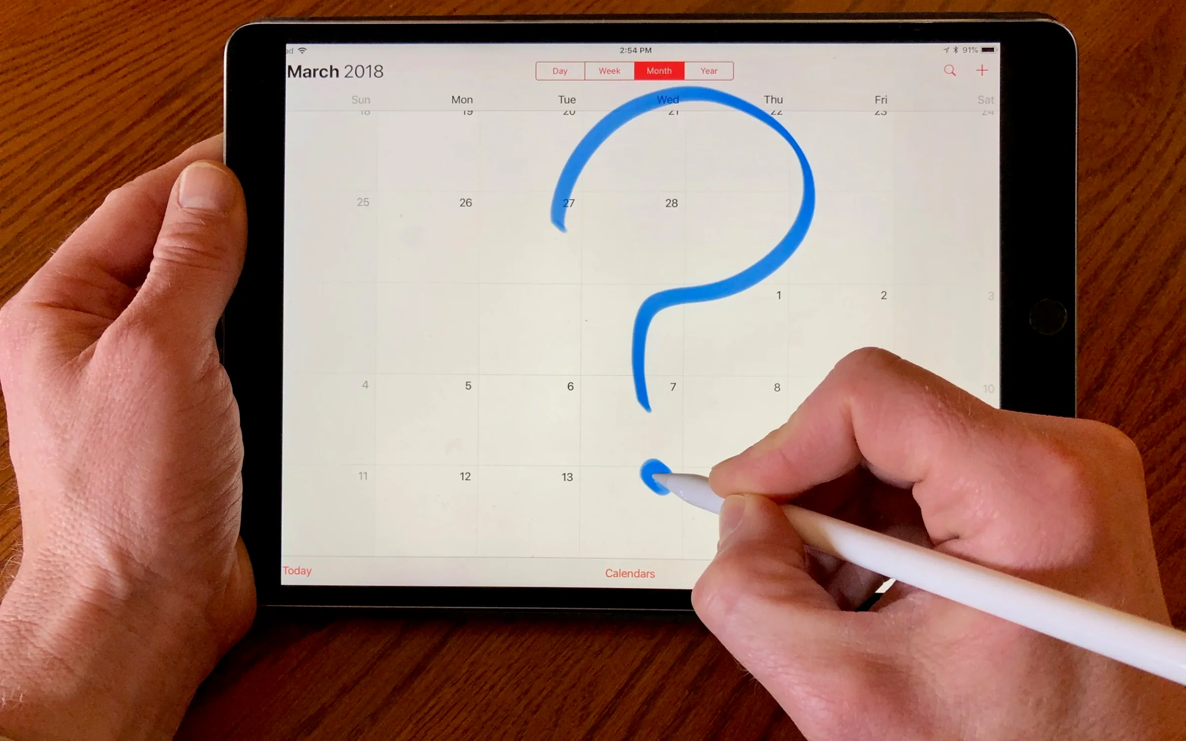 A hand using an Apple Pencil to draw a question mark over Calendar on an iPad