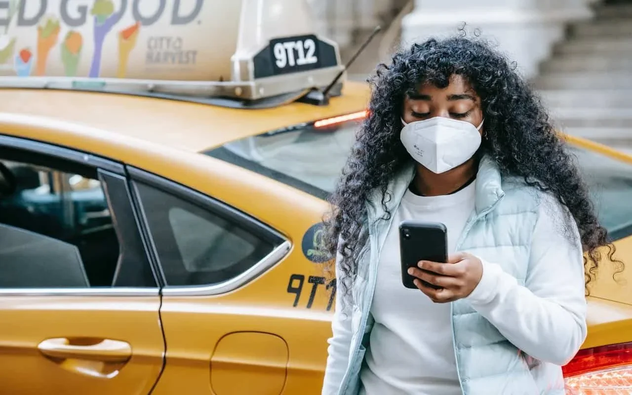 A masked woman using her iPhone beside a taxi