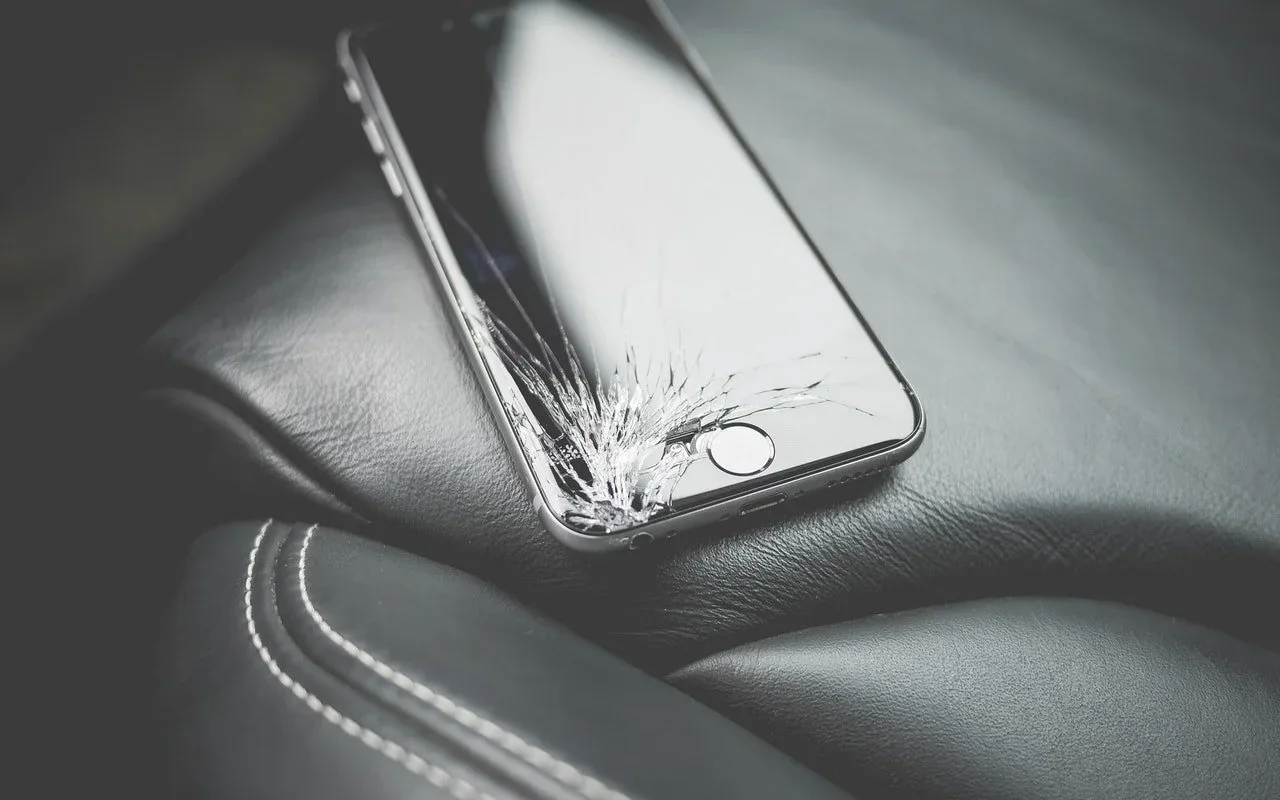 iPhone with a shattered screen resting on a car seat