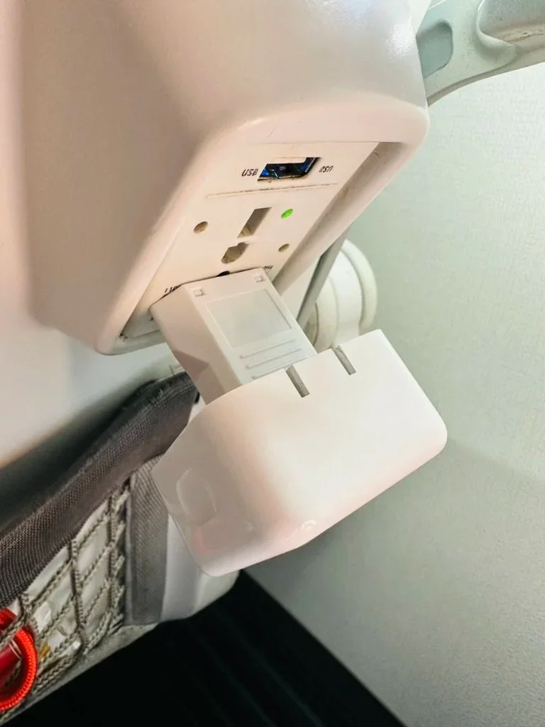A MacBook Air charger connected securely to a recessed airplane outlet using a Europlug adapter